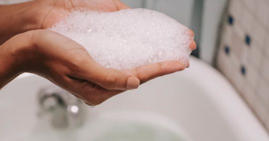 Hænder med sæbeskum over et fyldt badekar